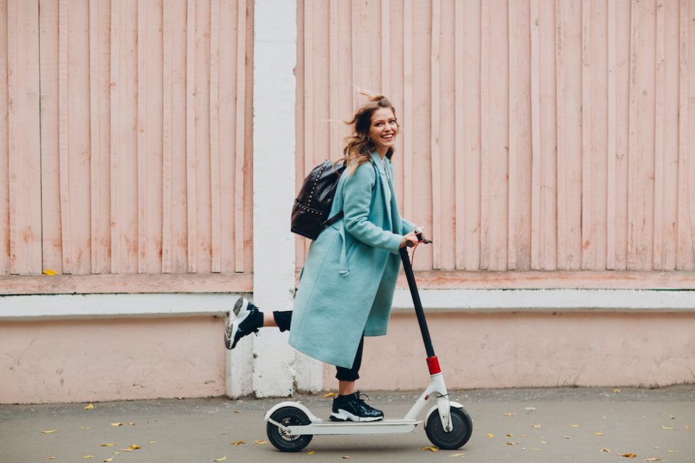 Young woman with electric scooter in blue coat at the city